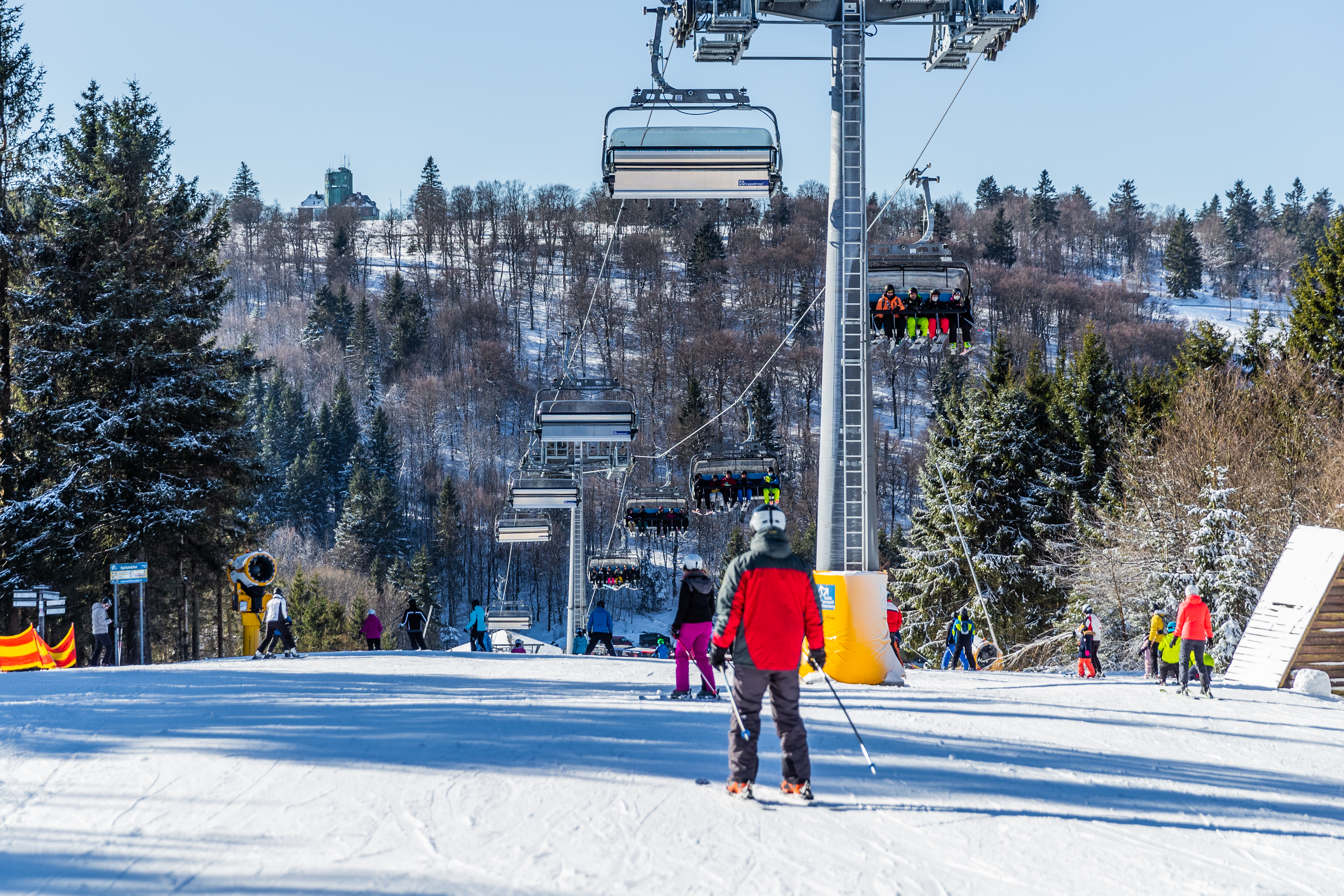 Sessellift über einer Piste mit Skifahrern und Snowboardern.