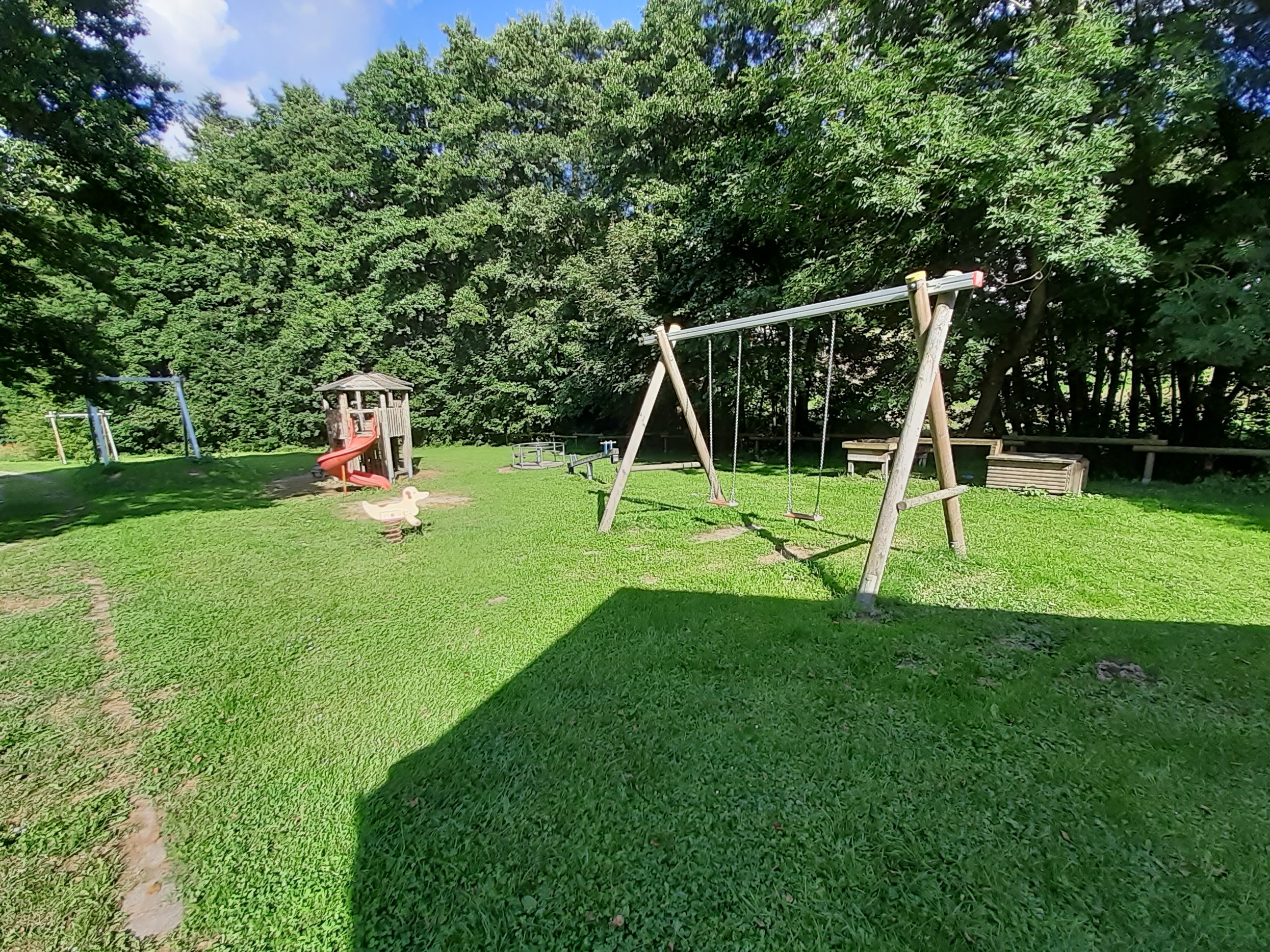 Spielplatz mit Schaukel und Klettergerüst mit Rutsche.