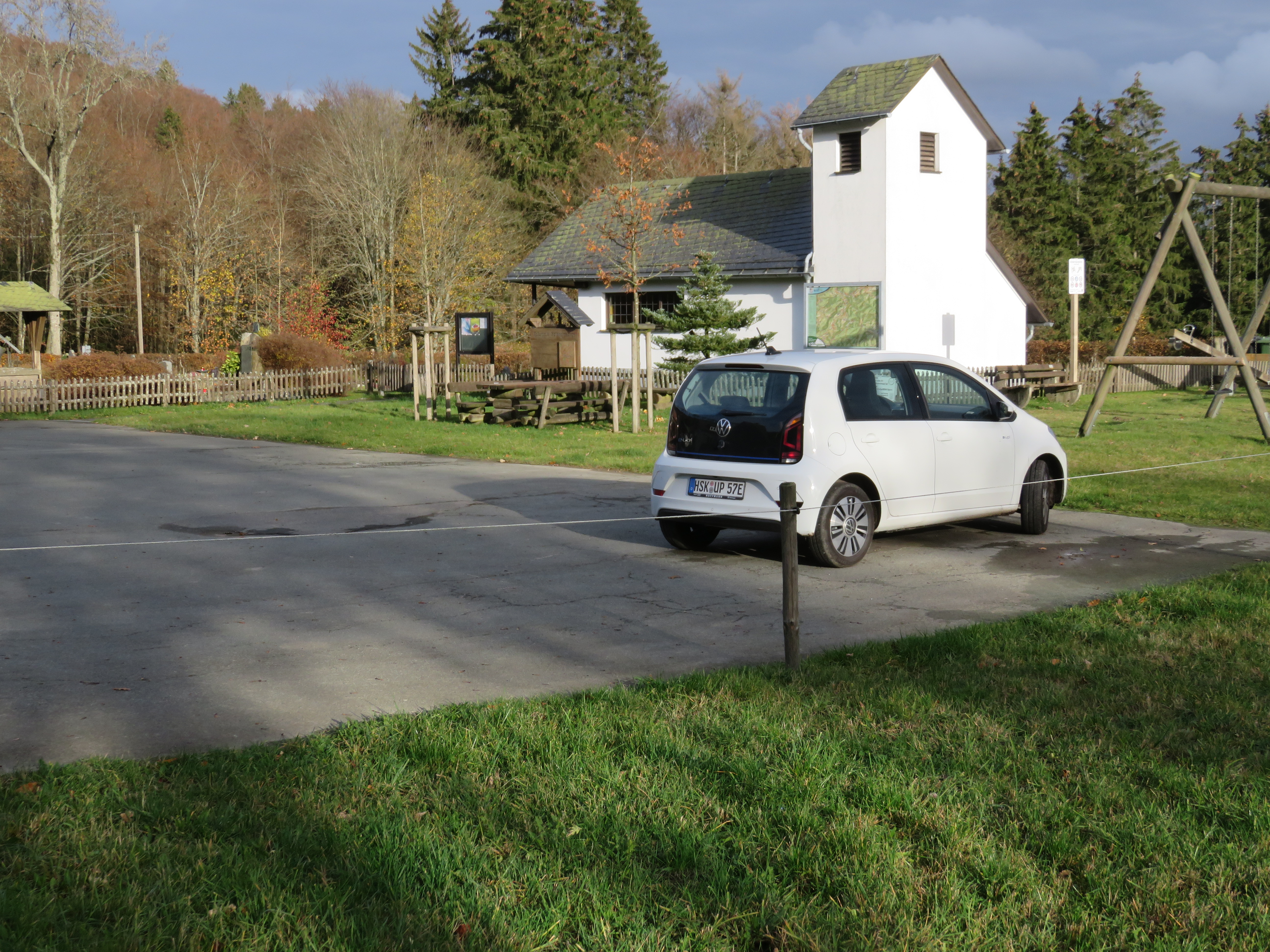 Parkplatz mit einem weißen geparkten Auto und einer kleinen Kapelle im Hintergrund.