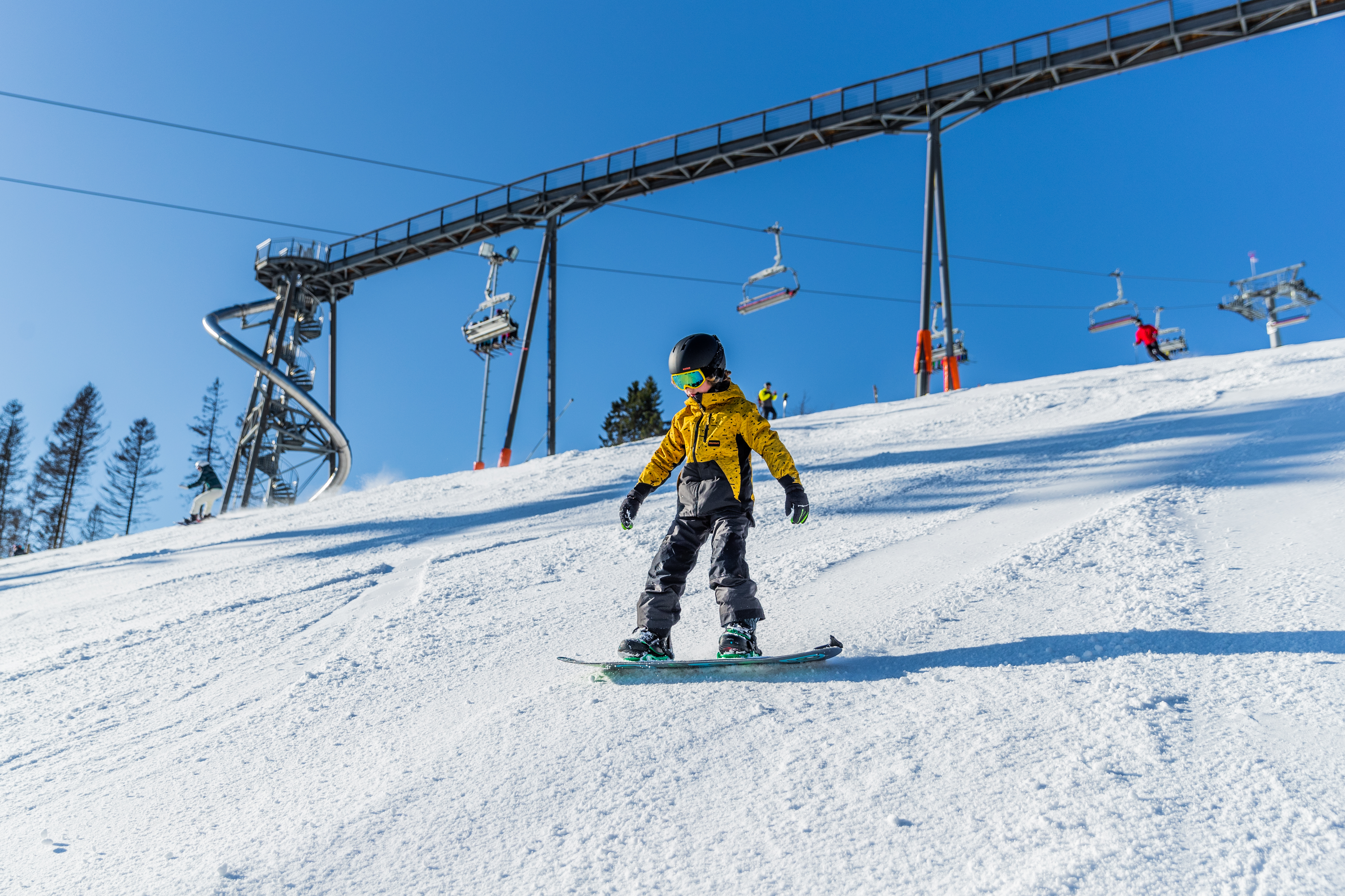 Ein Snowboardfahrer auf der Piste mit einem Sessellift und der Panorama Erlebnisbrücke im Hintergrund.