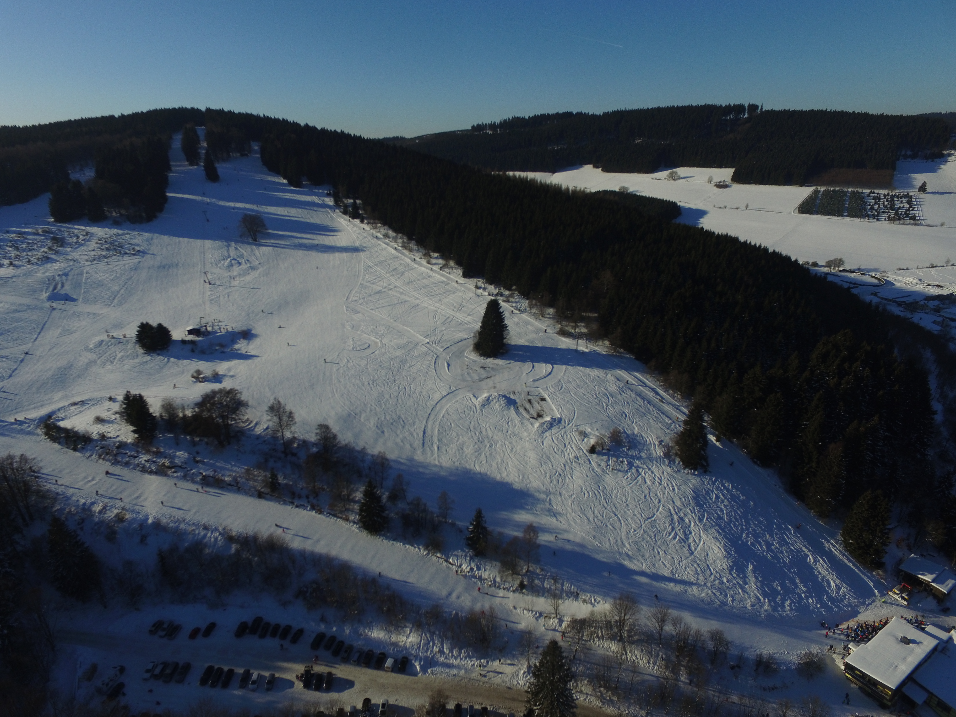 Drohnenaufnahme eines Skihangs mit Skilift, umgeben von Wäldern.