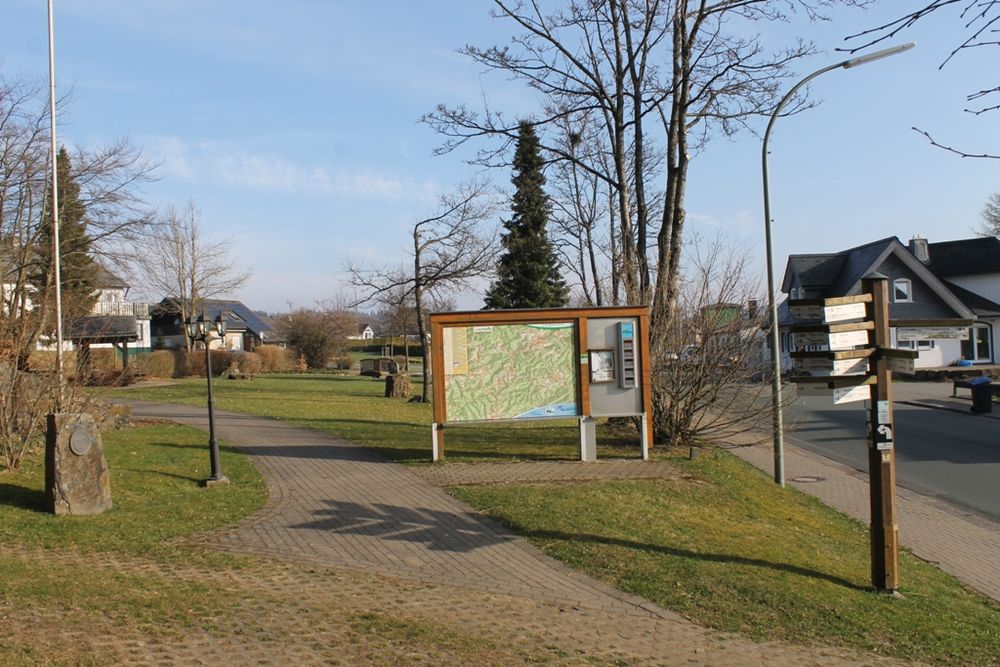 Informationstafel mit Wanderwegen neben einem Gehweg.