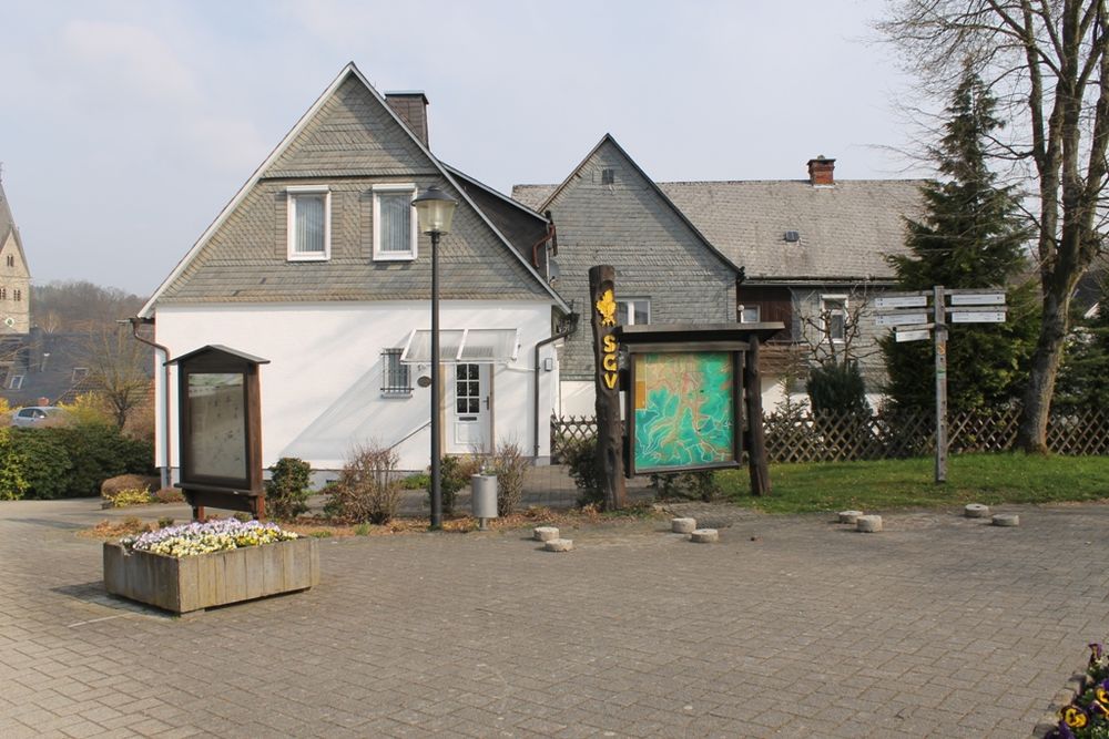 Informationstafel mit Wanderkarte mit Häusern im Hintergrund.