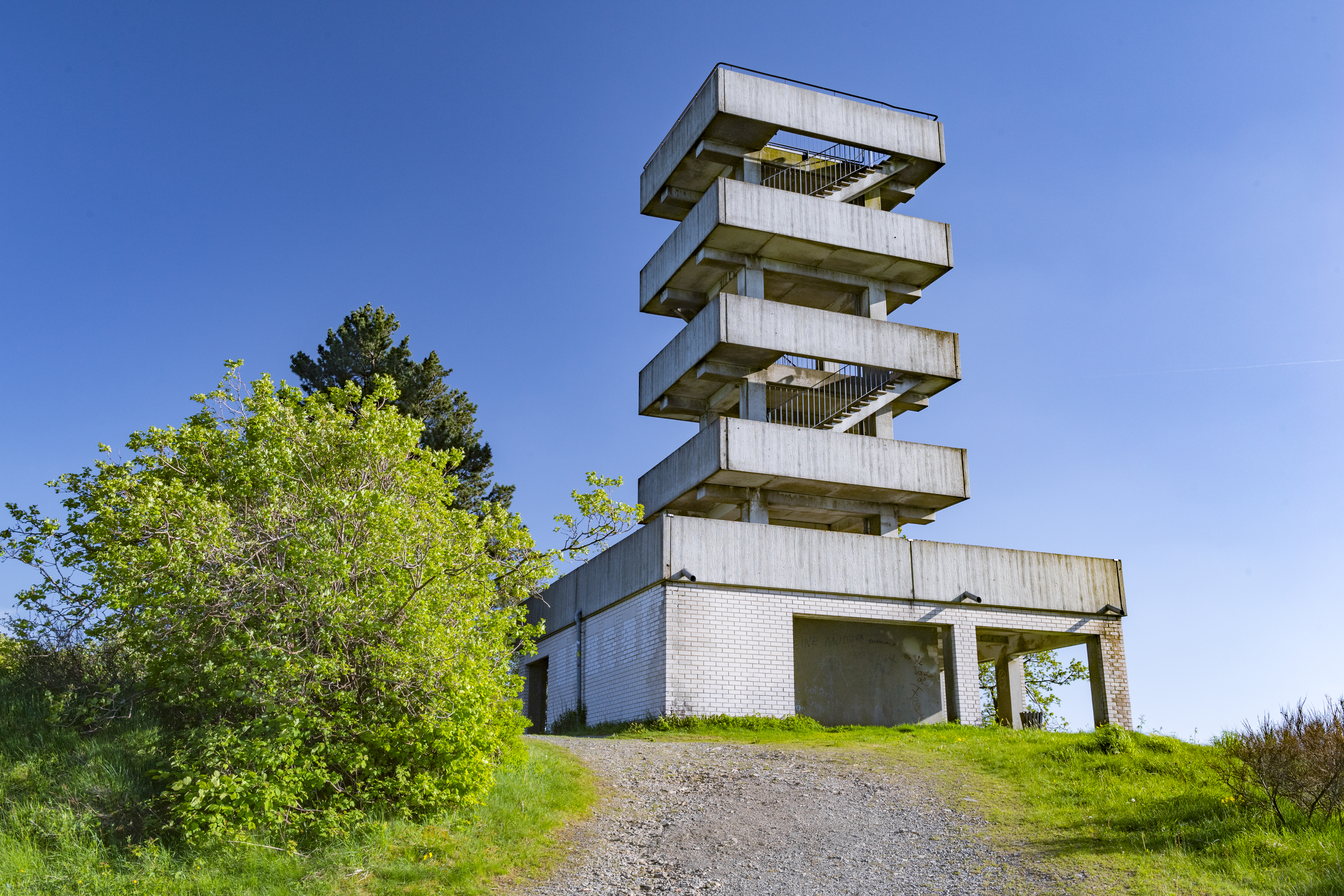 Turm aus Beton mit mehreren Etagen und Treppenaufgängen vor blauem Himmel.