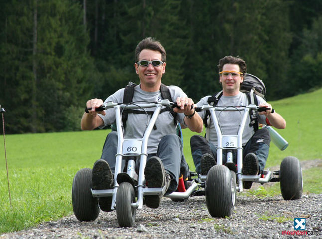 Zwei Männer fahren auf Mountaincarts, Fahrzeuge mit drei Rädern und einem Lenker, einen Weg entlang. Zwei Männer fahren auf Mountaincarts, Fahrzeuge mit drei Rädern und einem Lenker, einen Weg entlang.