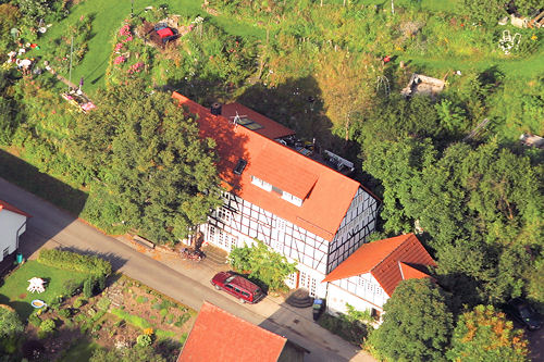 Drohnenaufnahme eines Fachwerkgebäudes inmitten von Wiesen und Bäumen.