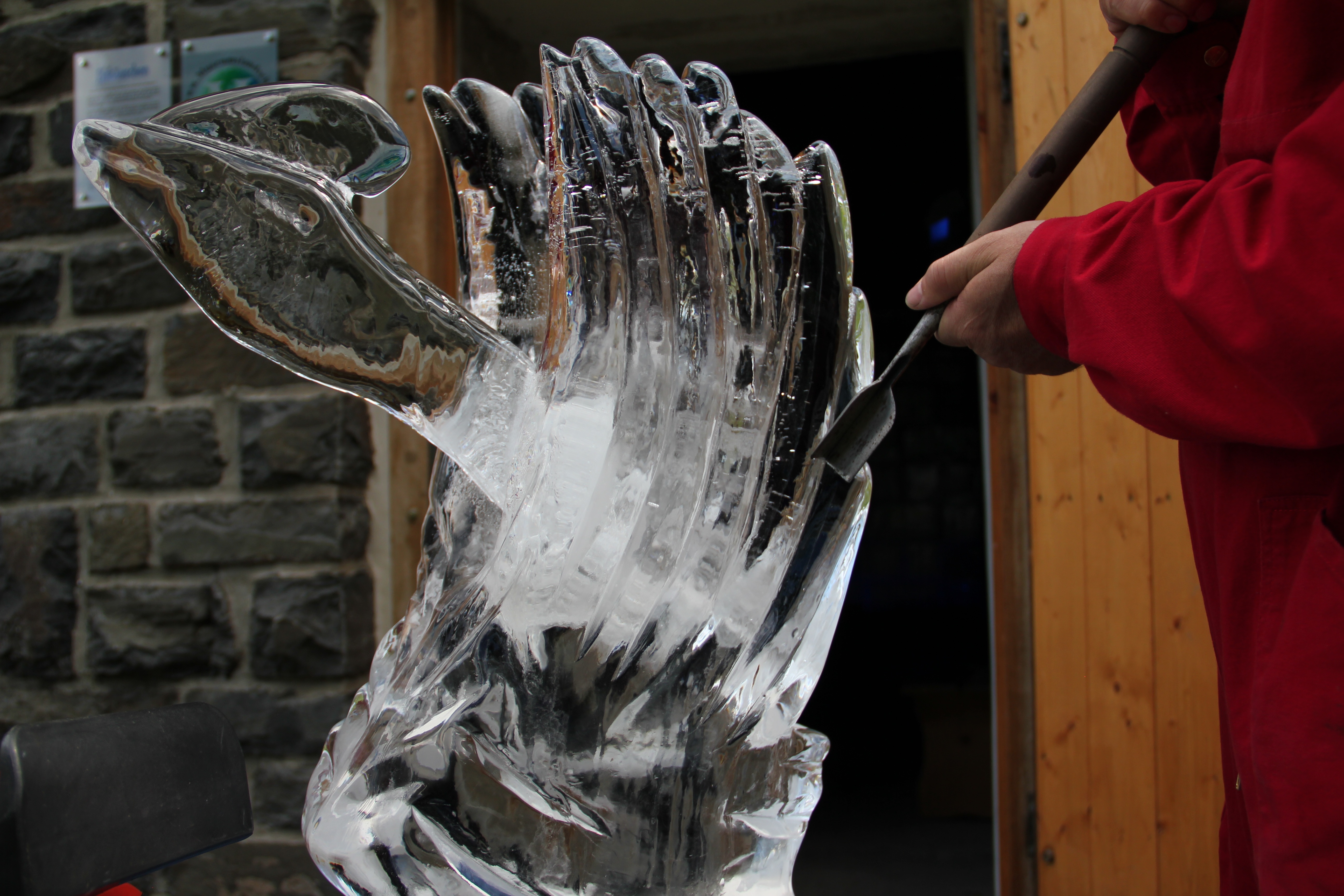Eine Person schnitzt mit einem Werkzeug eine Skulptur aus einem Eisblock. Eine Person schnitzt mit einem Werkzeug eine Skulptur aus einem Eisblock.