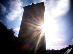 Ein hoher Turm vor blauem Himmel und Sonne.