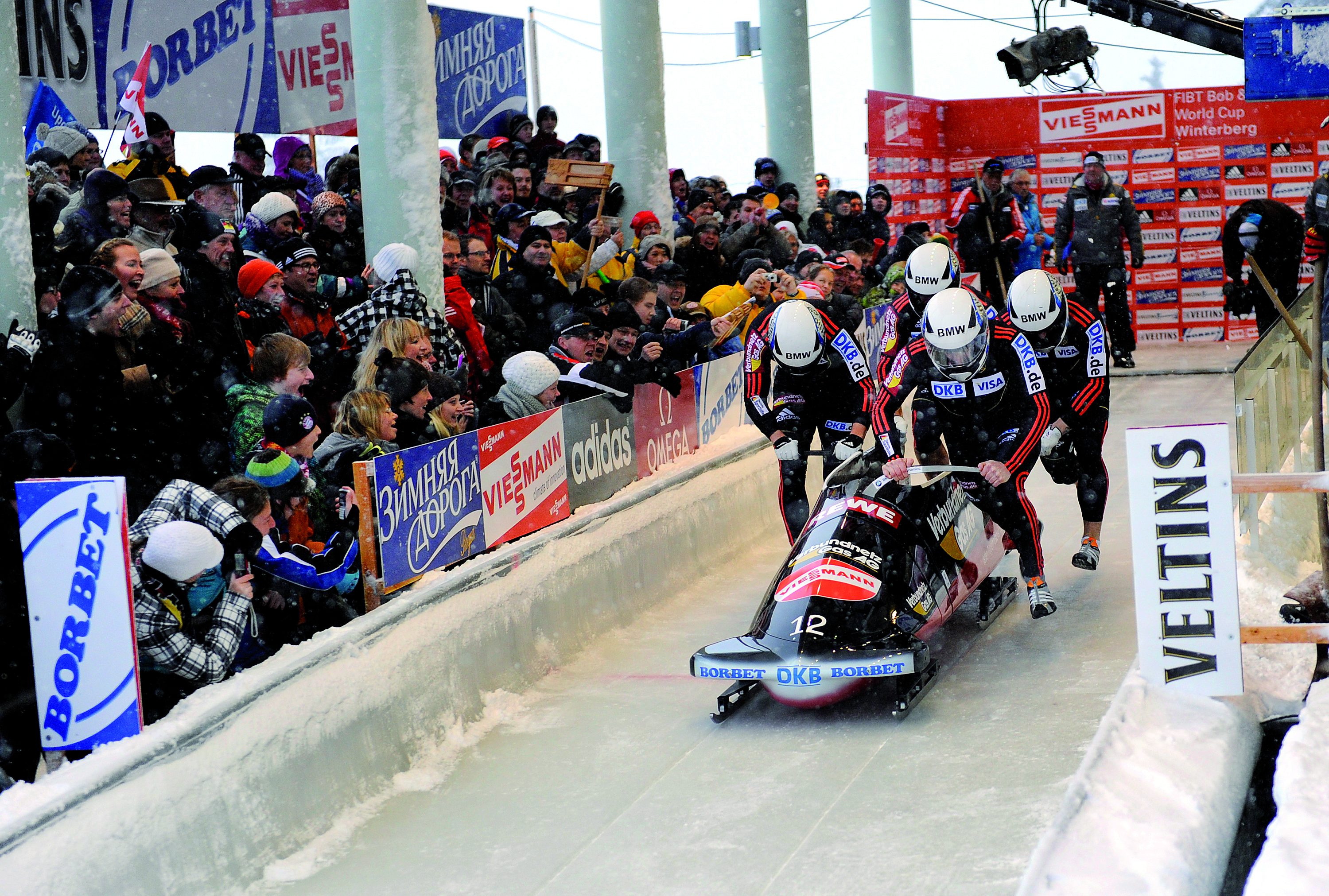 Das Team eines Viererbobs schiebt seinen Bob beim Start an und wird von den Zuschauern angefeuert. Das Team eines Viererbobs schiebt seinen Bob beim Start an und wird von den Zuschauern angefeuert.