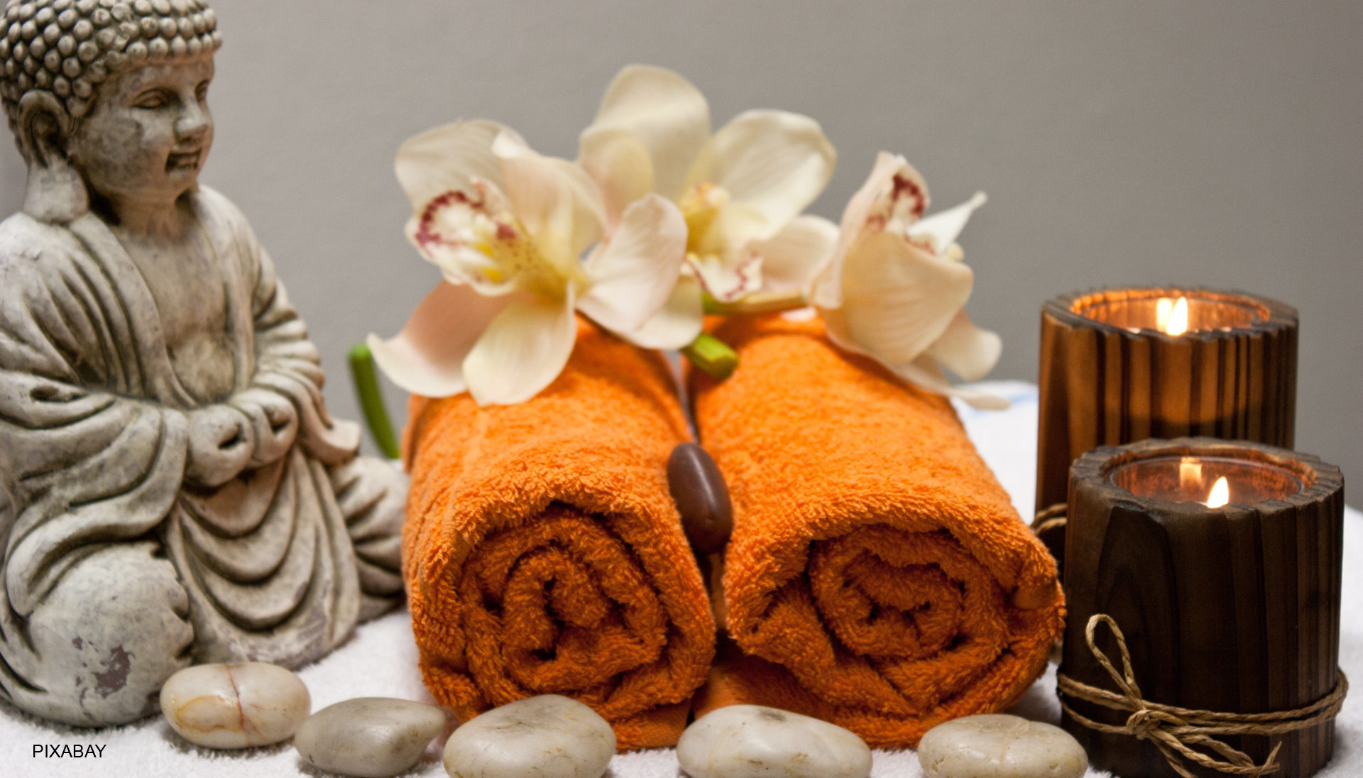 Zwei zusammengerollte Handtücher neben einer Buddha-Figur und Teelichtern, dekoriert mit Blüten.
