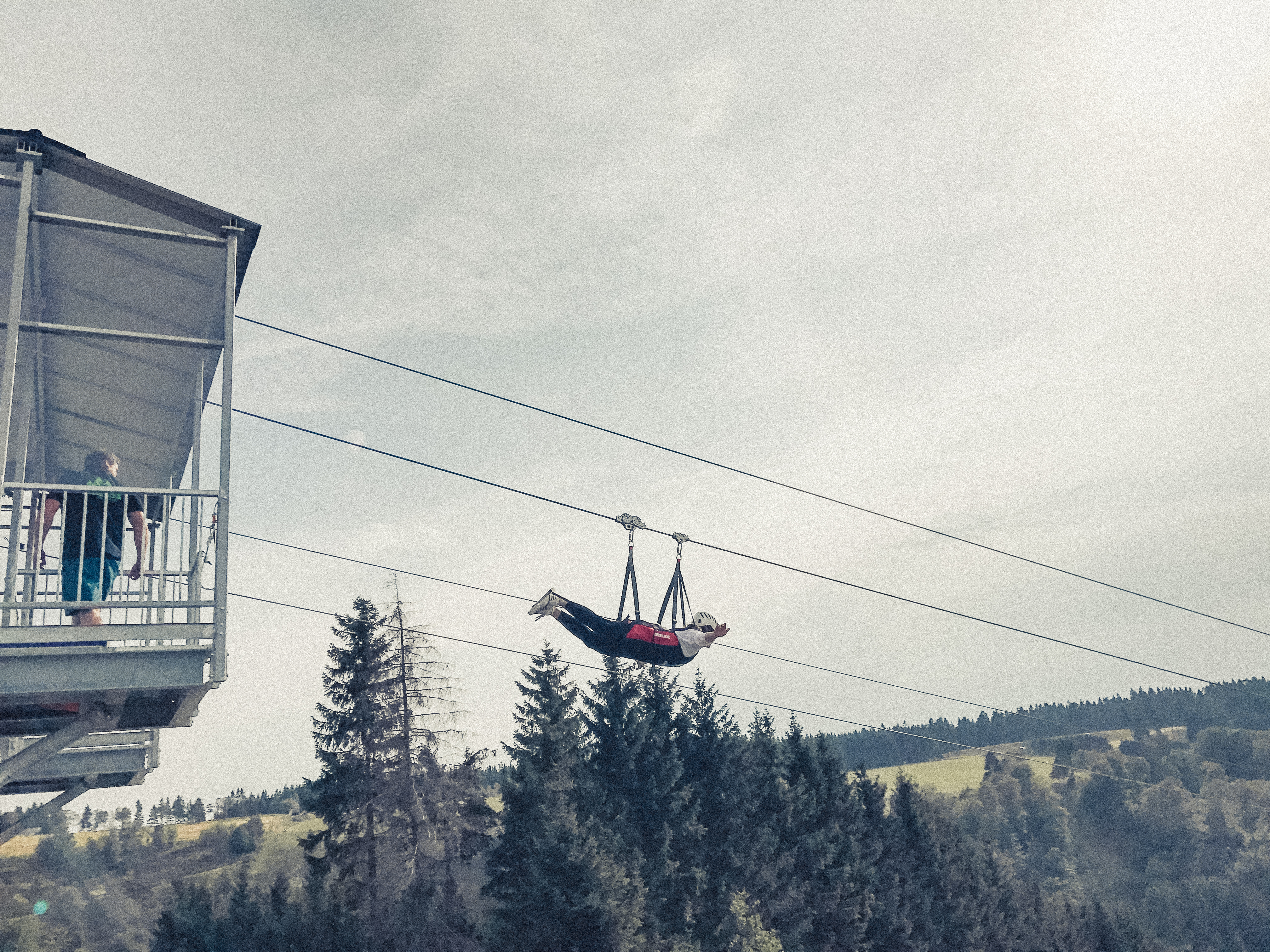Eine Person fliegt in einem Liegegurt eine Zipline hinunter. Eine Person fliegt in einem Liegegurt eine Zipline hinunter.