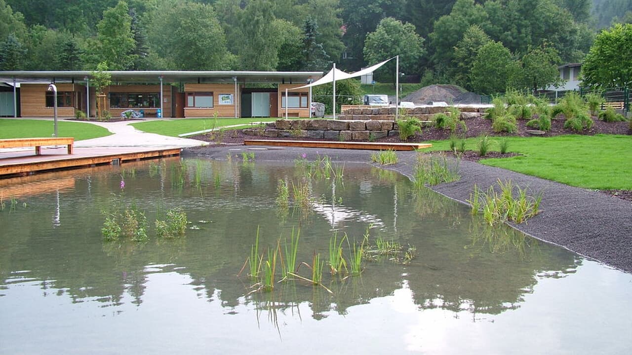 Ein Schwimmbecken mit angrenzender Liegewiese und einem Gebäude im Hintergrund. Ein Schwimmbecken mit angrenzender Liegewiese und einem Gebäude im Hintergrund.