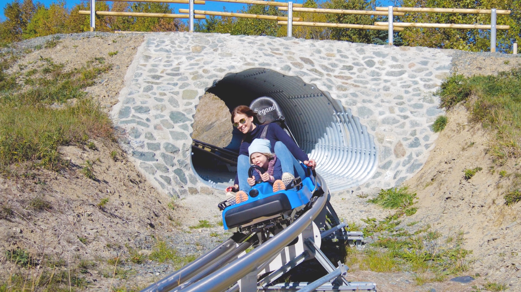 Mutter mit Kind fährt auf einem Schlitten die Sommerrodelbahn hinunter. Mutter mit Kind fährt auf einem Schlitten die Sommerrodelbahn hinunter.