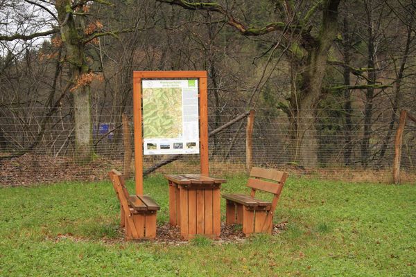 Ein Tisch mit zwei Bänken vor einem Infoschild auf einer Wiese. Ein Tisch mit zwei Bänken vor einem Infoschild auf einer Wiese.