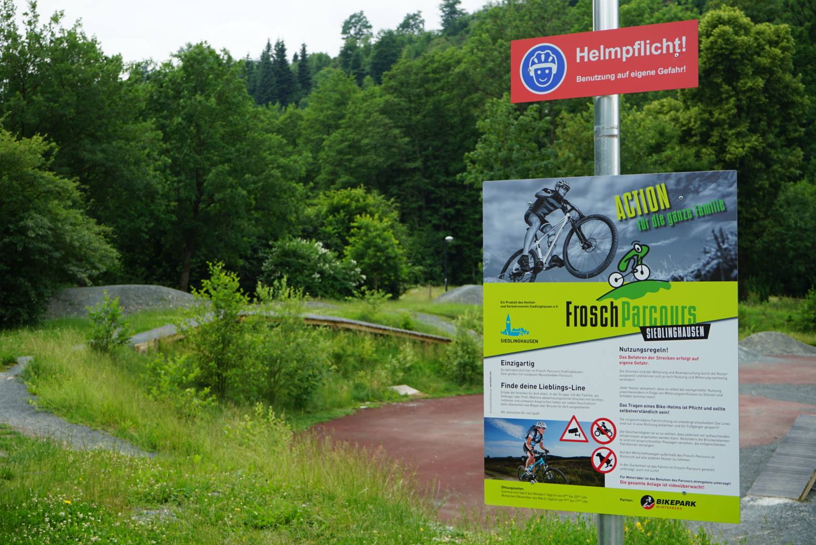 Kleiner Bikepark für Kinder mit einem Informationsschild zum Froschparcours im Vordergrund.