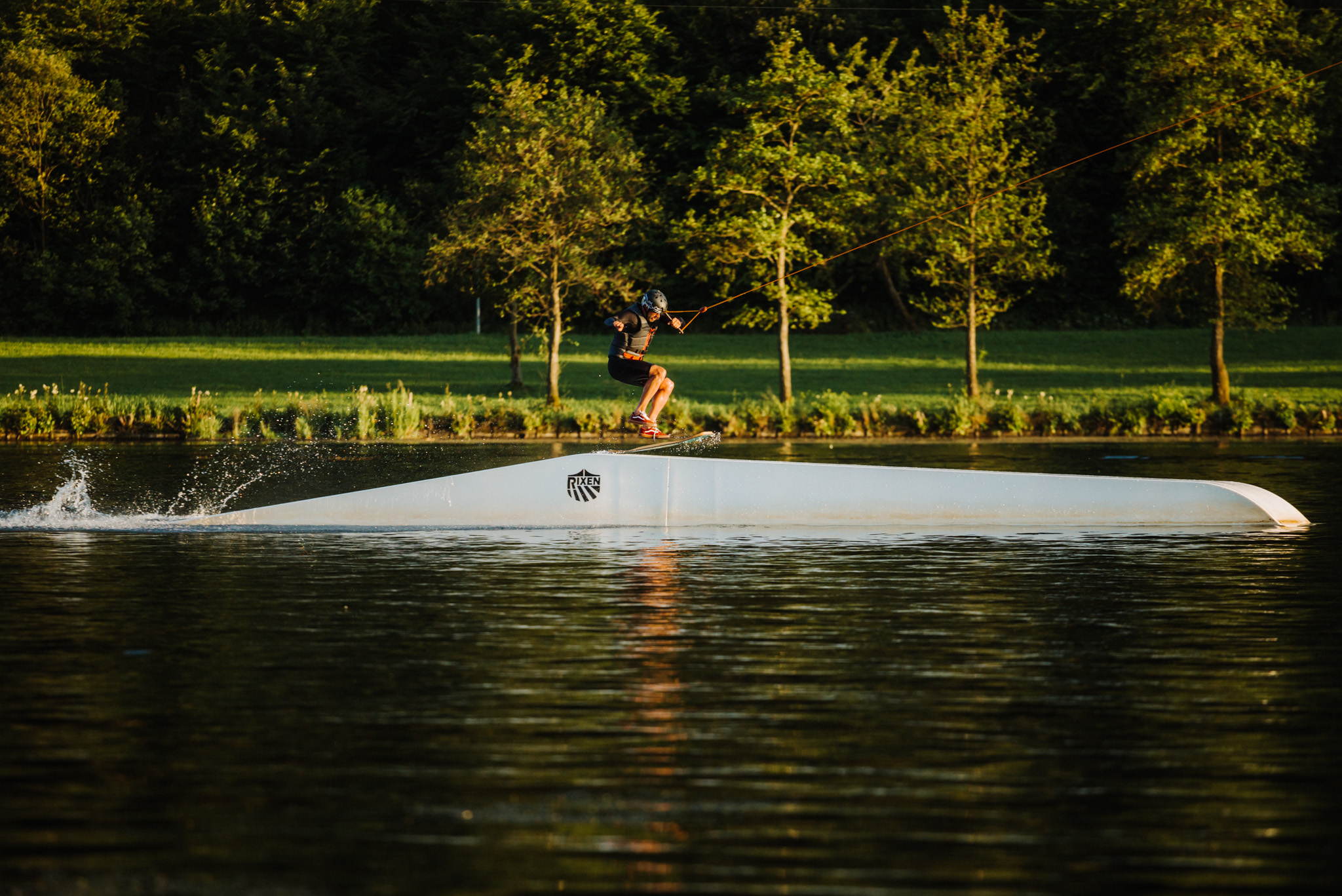 Ein Wasserskifahrer fährt über ein Sprungelement im See.