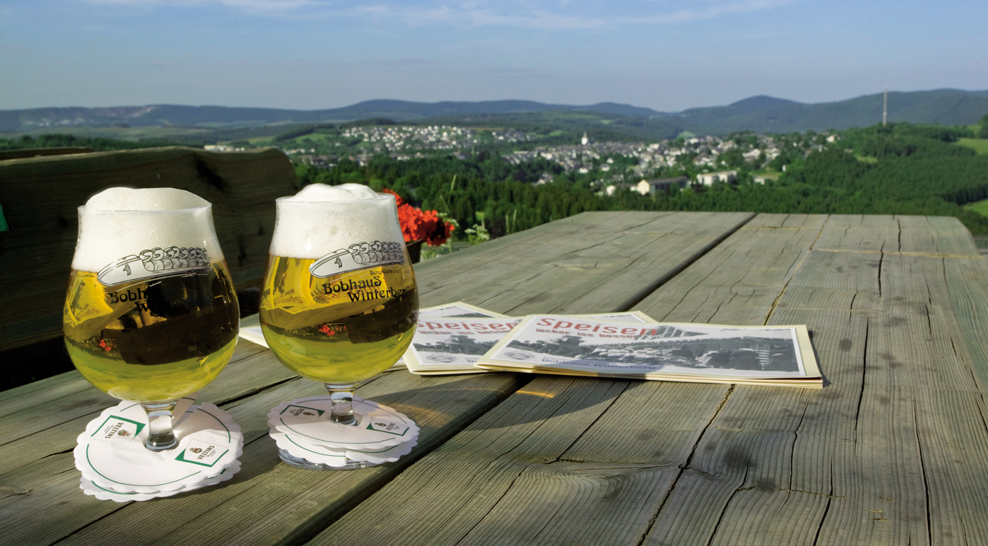 Zwei Biergläser auf einem Holztisch mit einer weiten Aussicht auf die Umgebung.