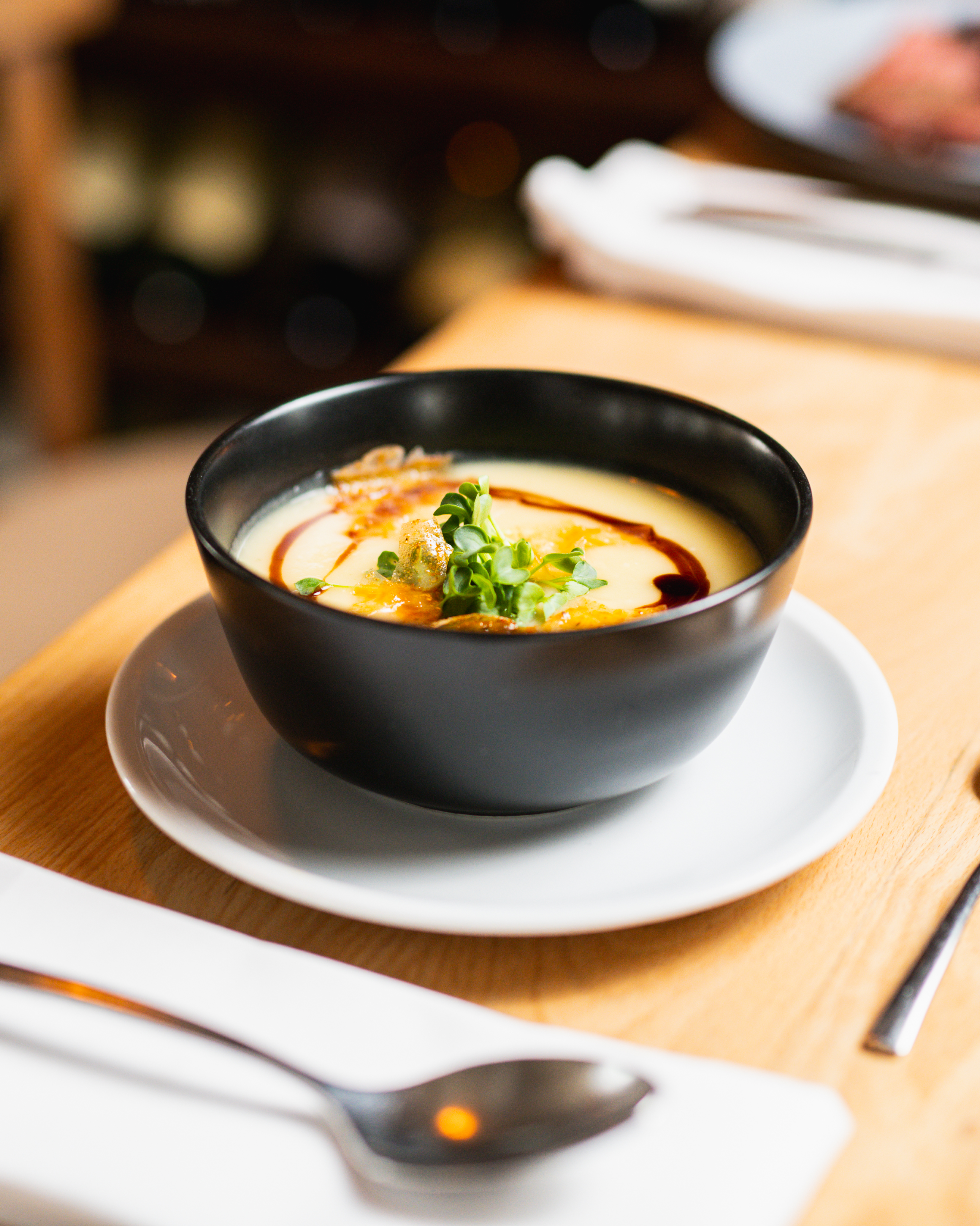 Eine Schale mit Suppe und einem Löffel daneben auf einem Tisch.