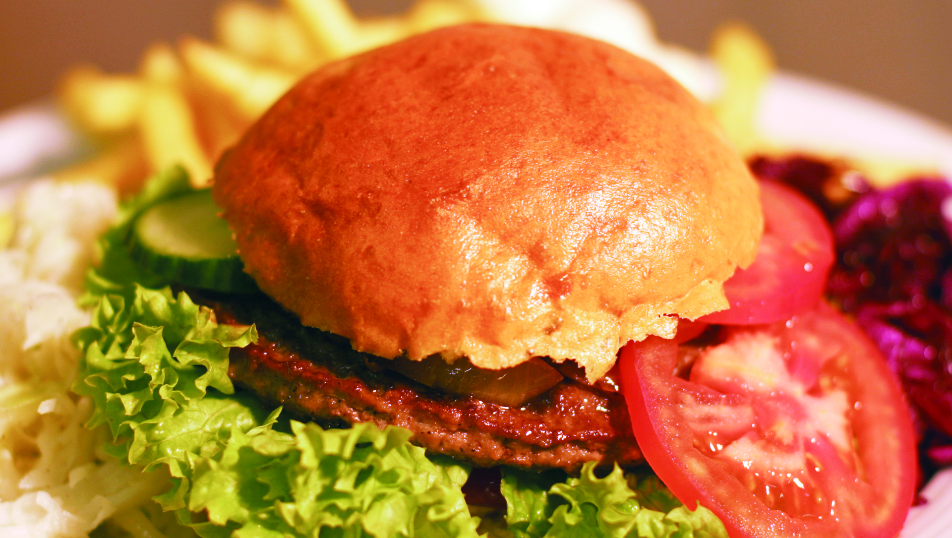 Großaufnahme eines Hamburgers mit Tomaten und Salat und Pommes im Hintergerund.