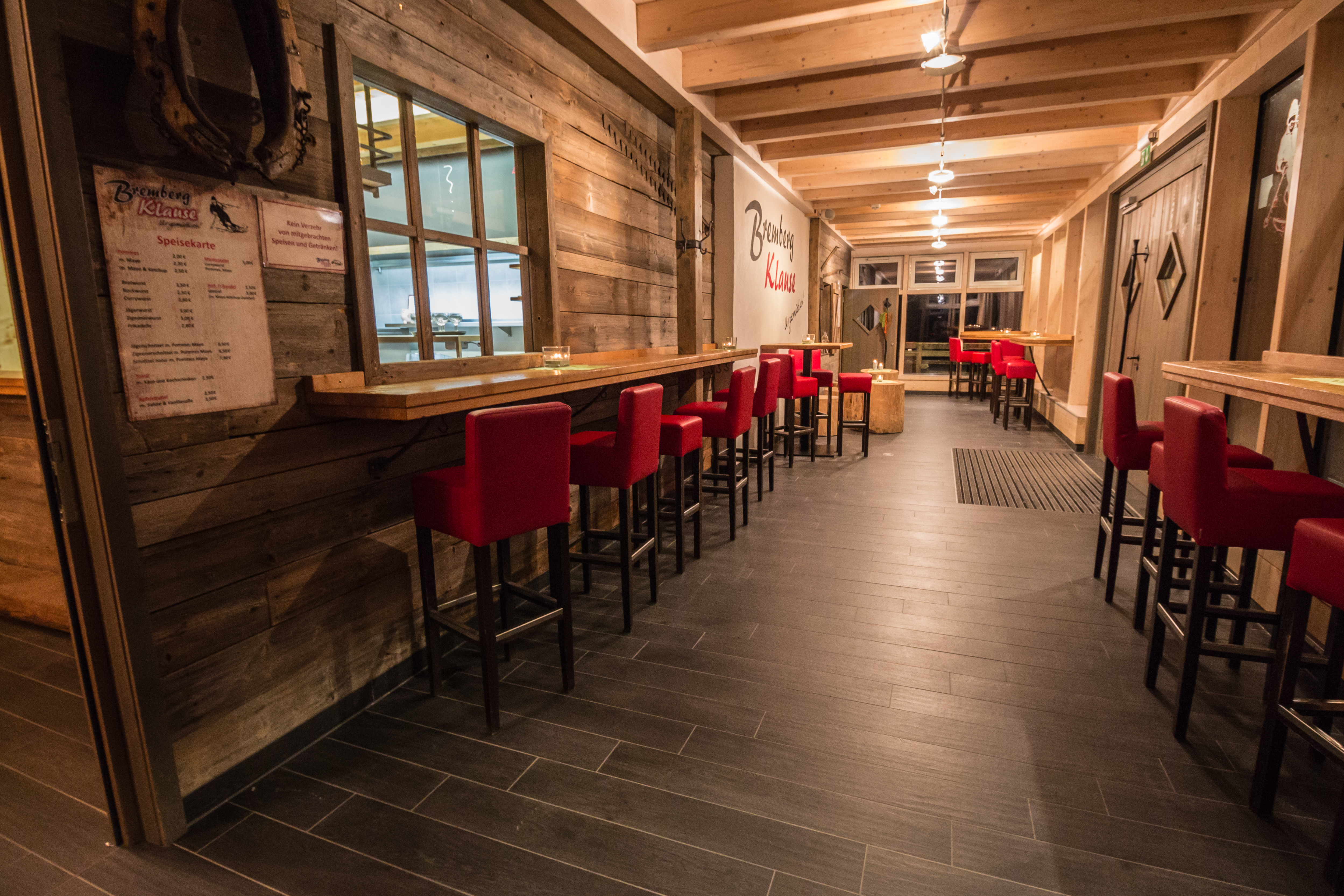 Ein langer Flur mit Tischen und hohen Stühlen an den hölzernen Wänden.