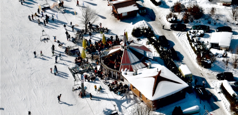 Drohnenaufnahme einer Skihütte im Winter mit einigen Personen im Außenbereich.