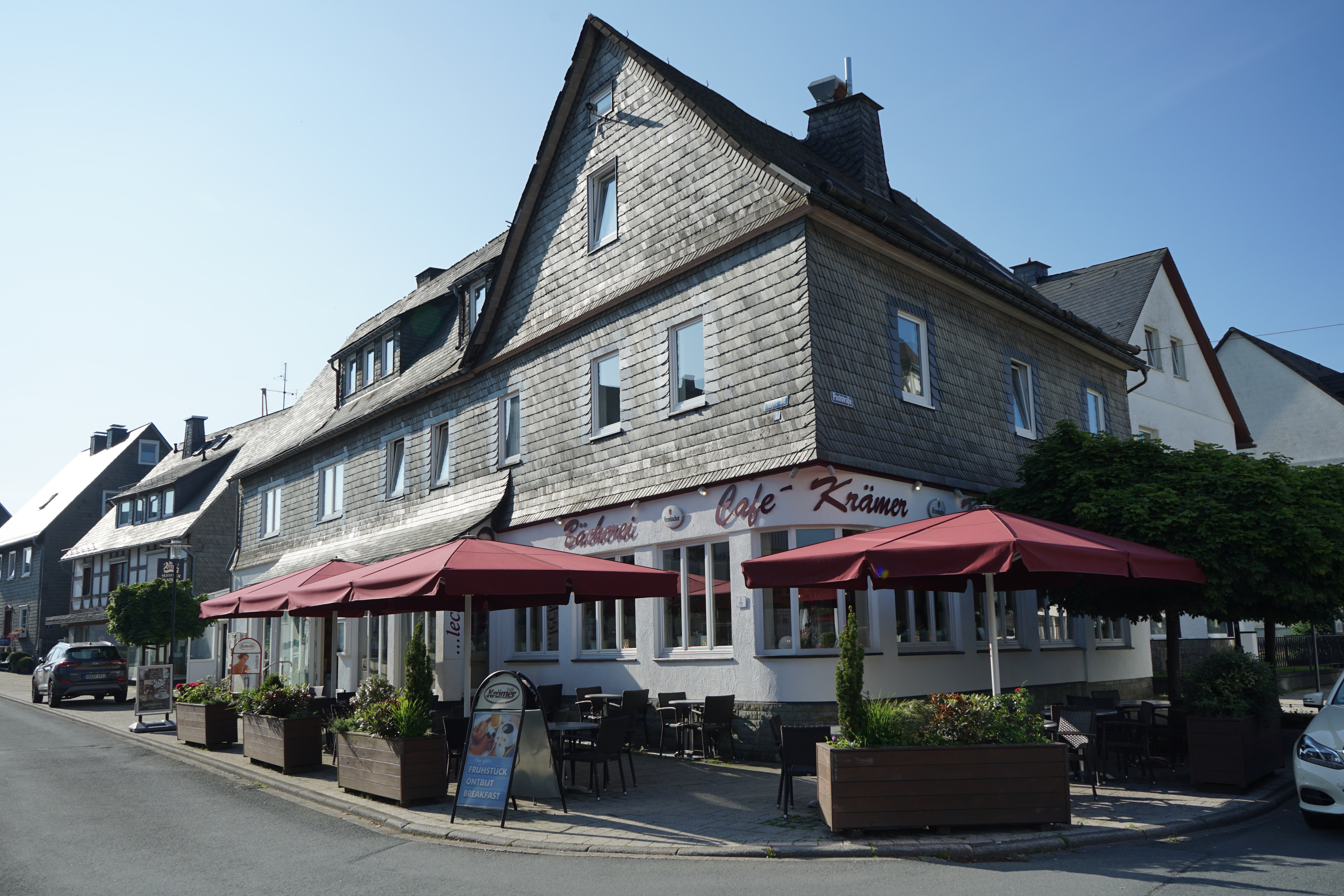 Eine Terrasse mit Sitzmöglichkeiten und Sonnenschirmen vor einem Gebäude mit der Aufschrift Café Krämer.