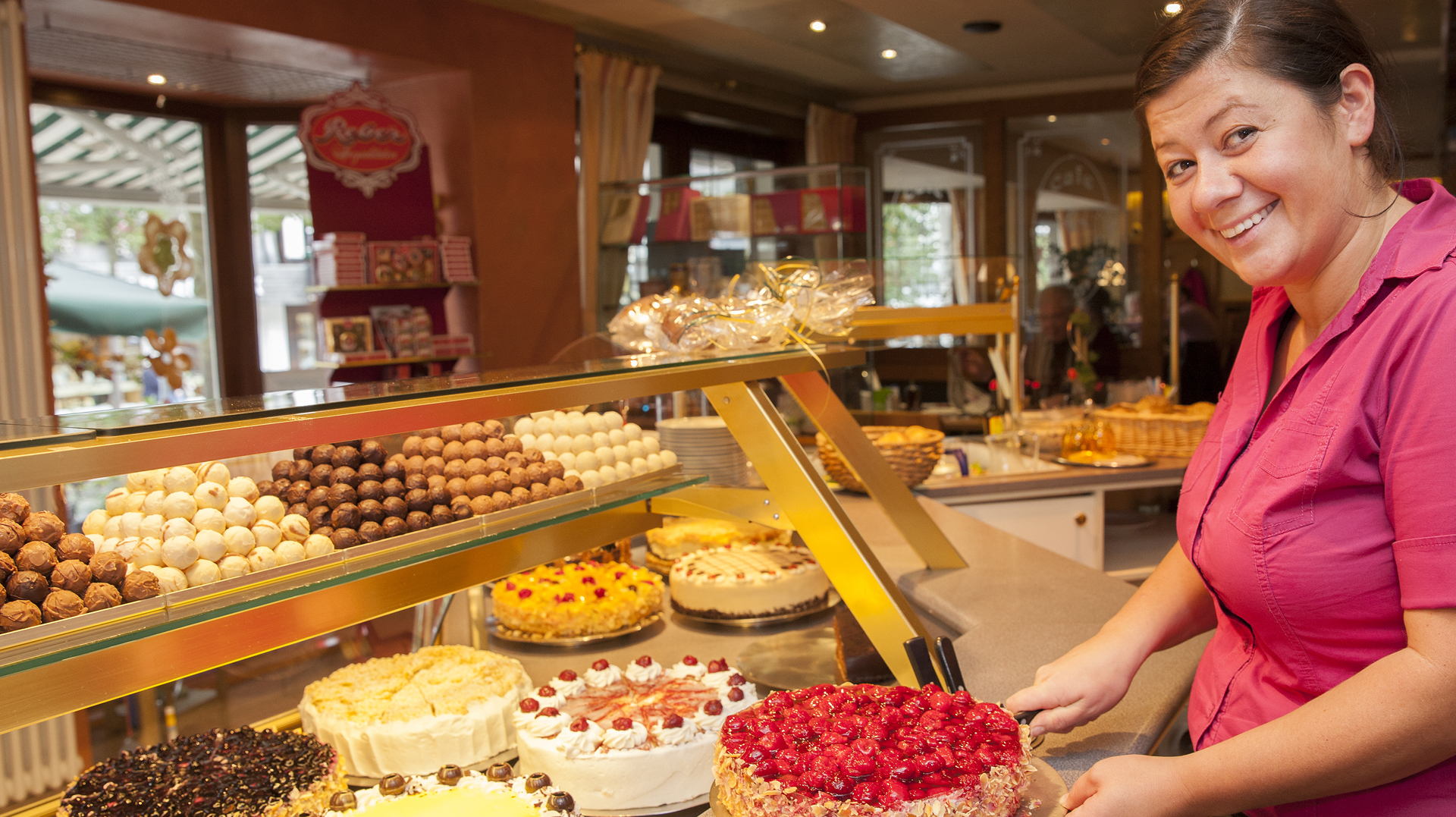 Eine Frau neben einer Kuchentheke voller Torten, Kuchen und Pralinen.