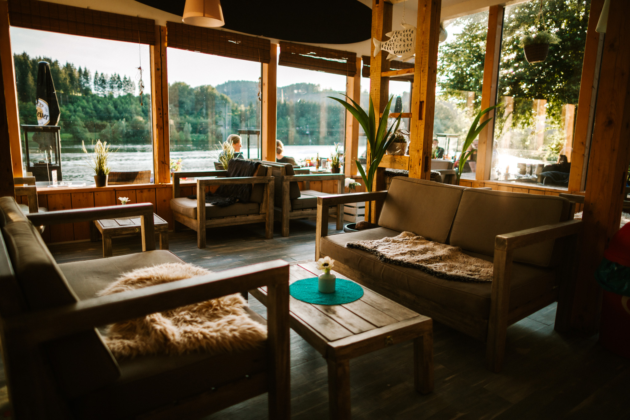 Ein mit gemütlichen Sitzmöbeln ausgestatter Innenraum mit großen Fenstern und Blick auf den Hillebachsee.