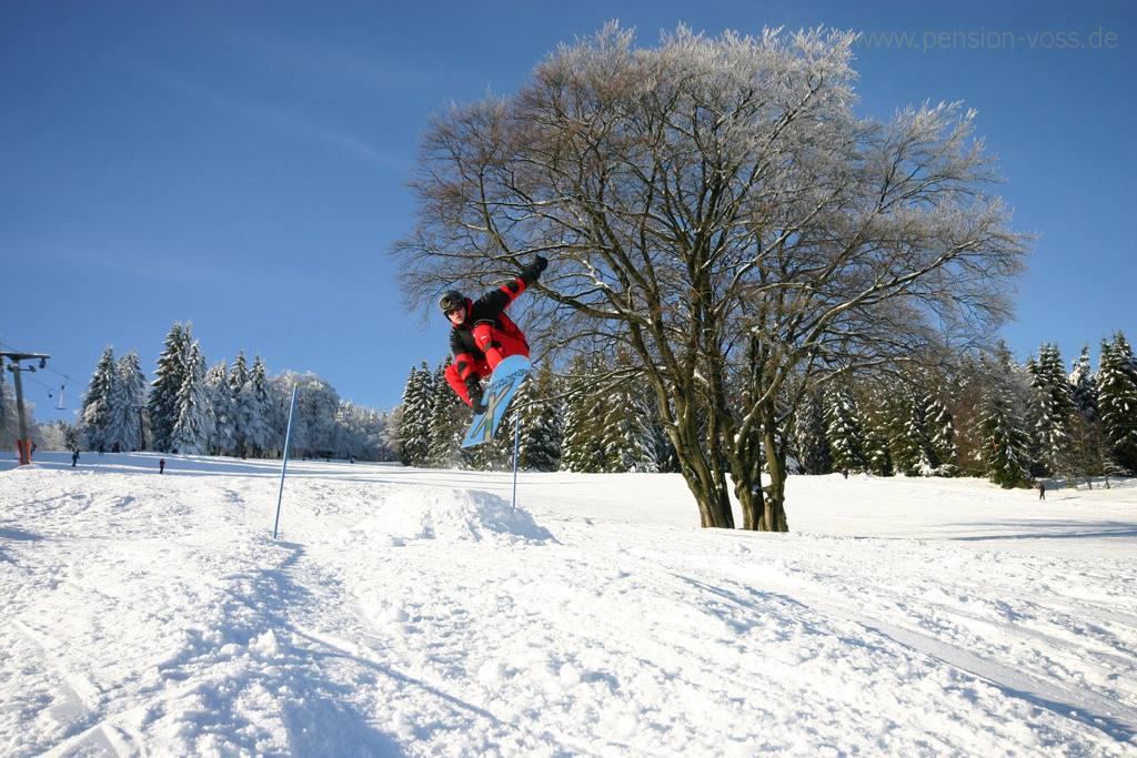 Ein Snowboardfahrer macht bei der Fahrt einen Sprung über eine Schneeschanze.
