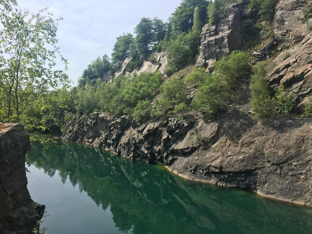 Ein Teil eines klaren Bergsees von Felswänden mit grünen Sträuchern umgeben.