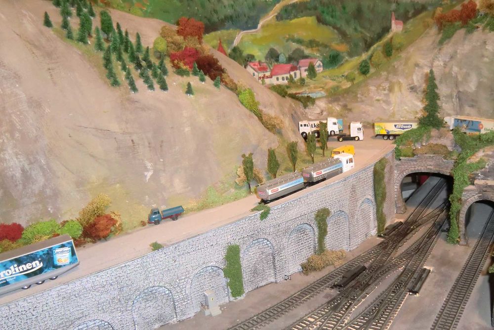 Eine Modellbahnanlage mit Bahngleisen, einem Tunnel und einer von LKWs befahrenen Straße.