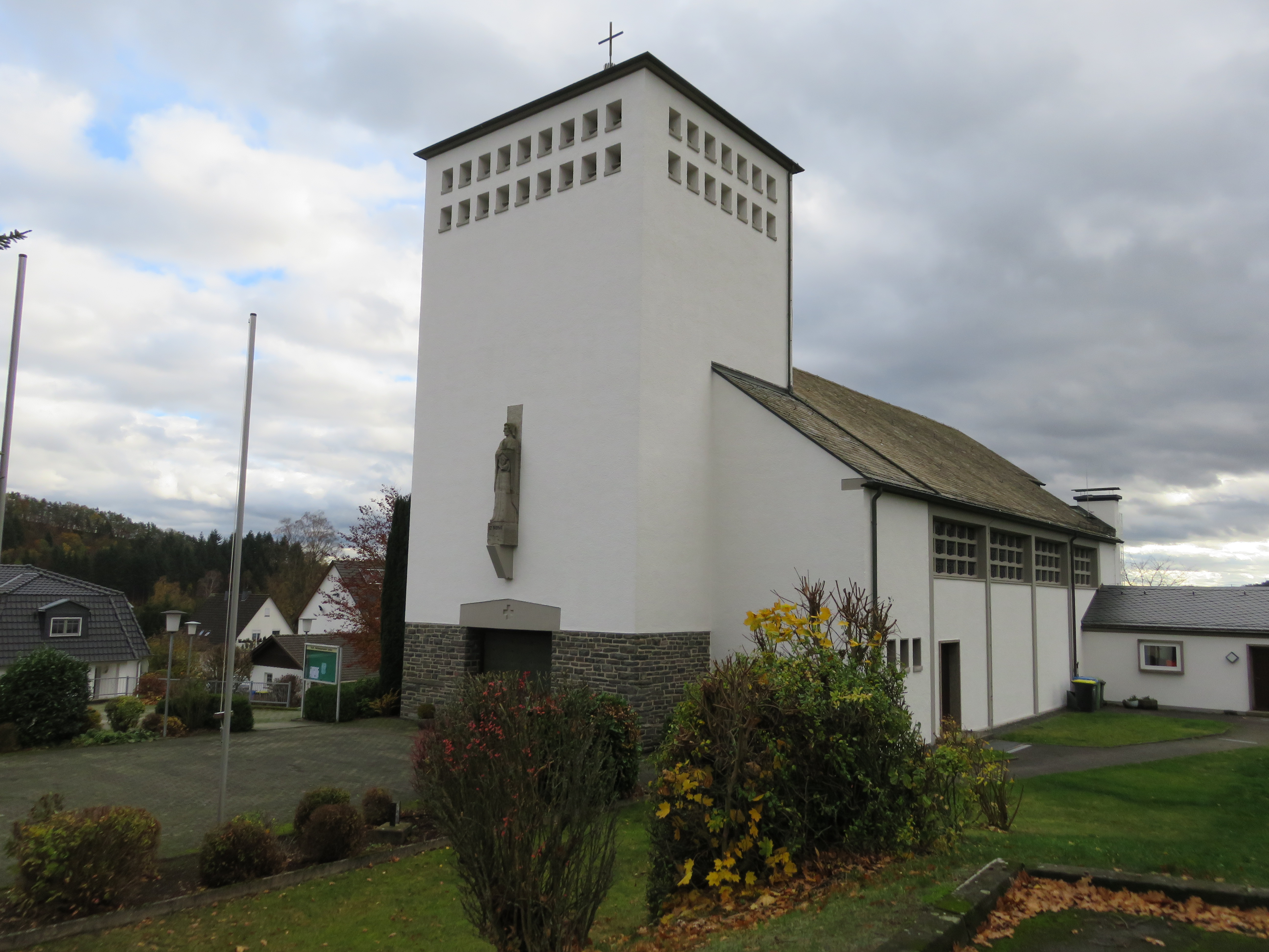 Eine Kirche vor bewölktem Himmel und ein paar Häusern im Hintergrund.