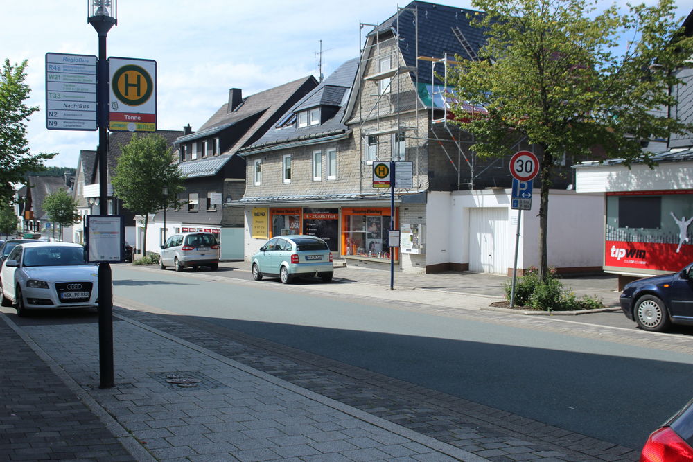 Ein Bushaltestellenschild an einer Straße mit parkenden Autos und Häusern.