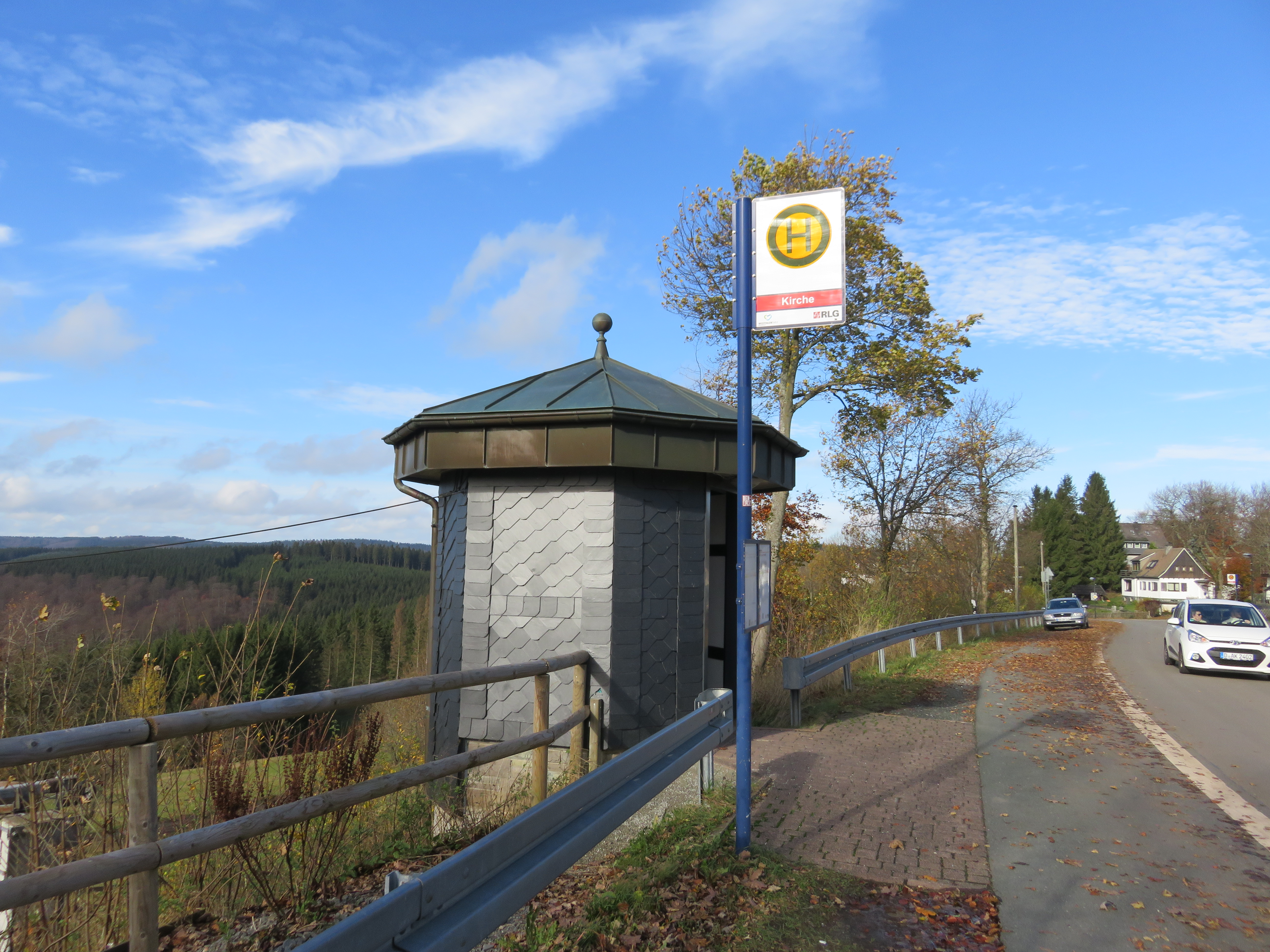 BEin Bushaltestellen-Häuschen mit einem Halteschild an einer Straße.