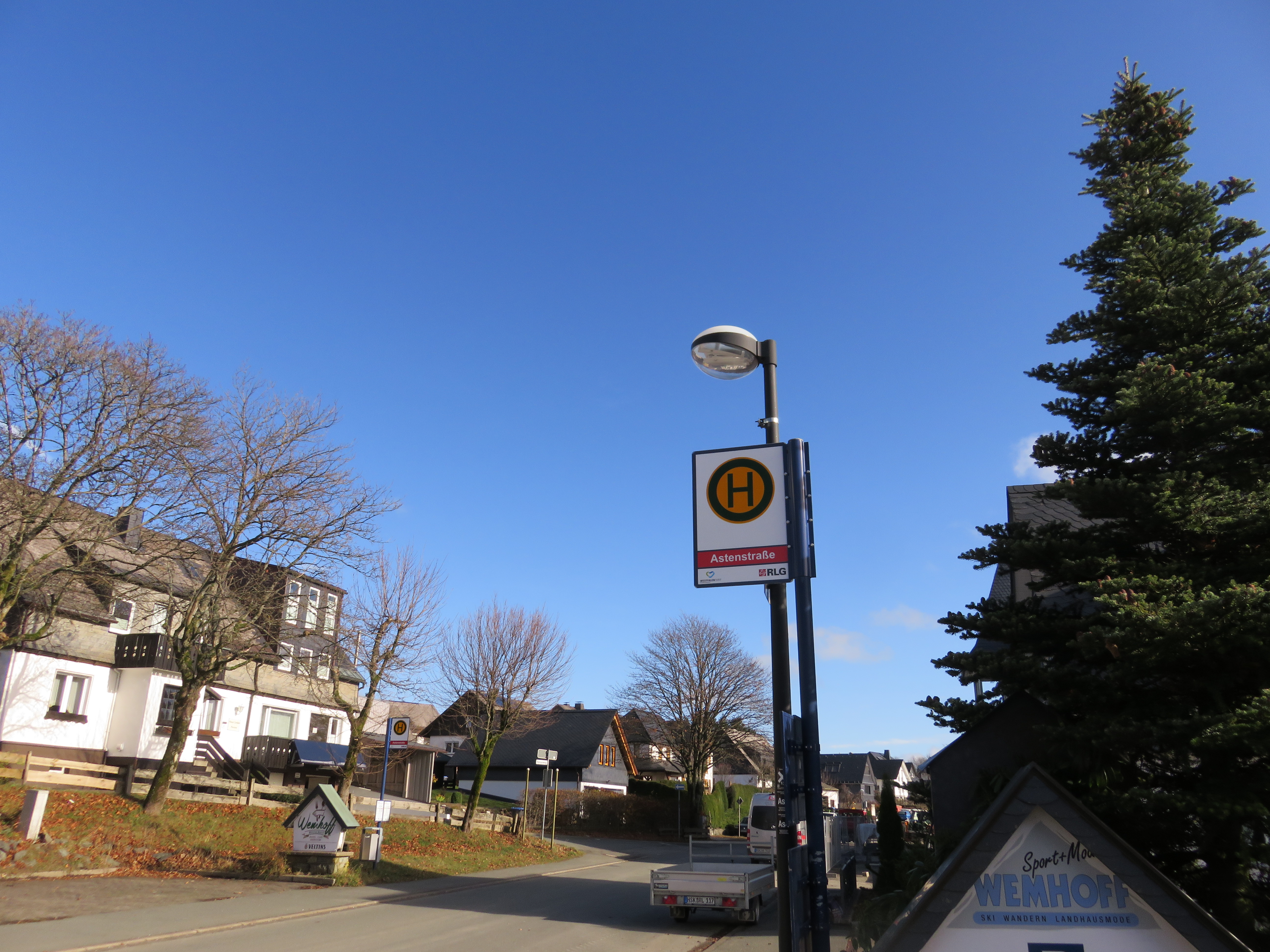Ein Bushaltestellenschild an einer Straße mit Häusern im Hintergrund.