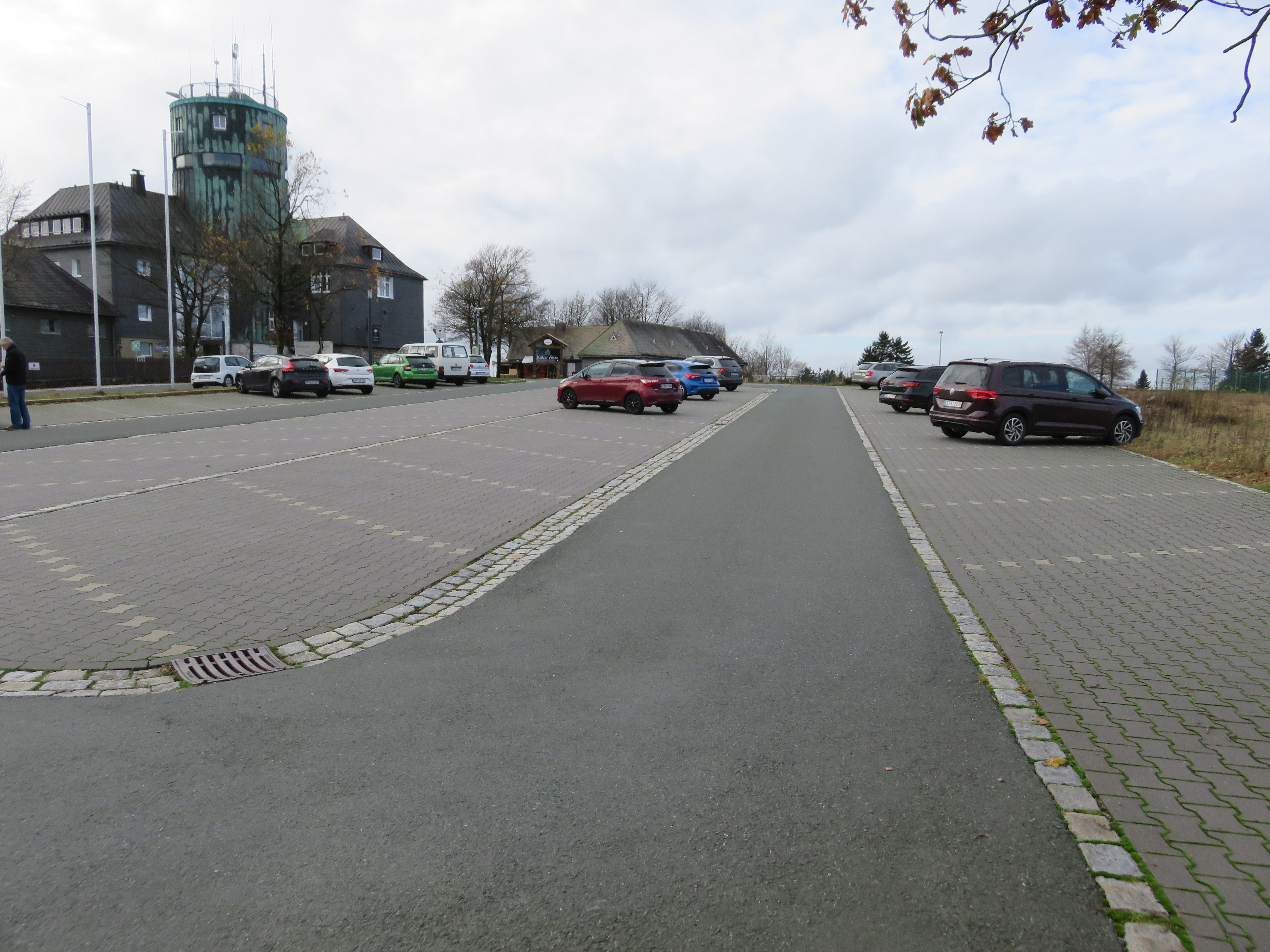 Gepflasterte Parkmöglichkeiten rechts und links von einer Asphaltstraße mit dem Astenturm im Hintergrund.