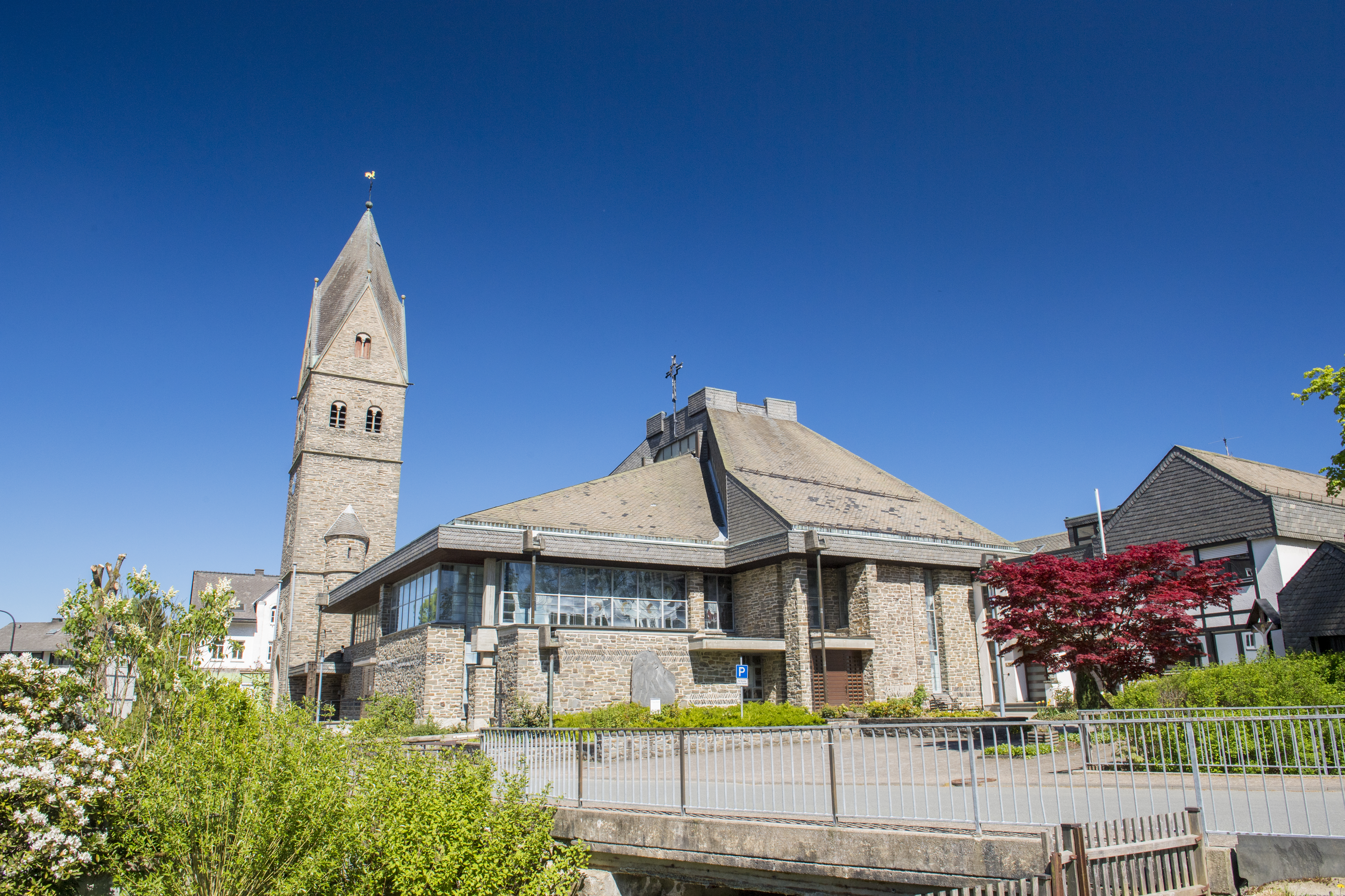 Eine Kirche vor blauem Himmel mit Bäumen und Sträuchern im Vordergrund.