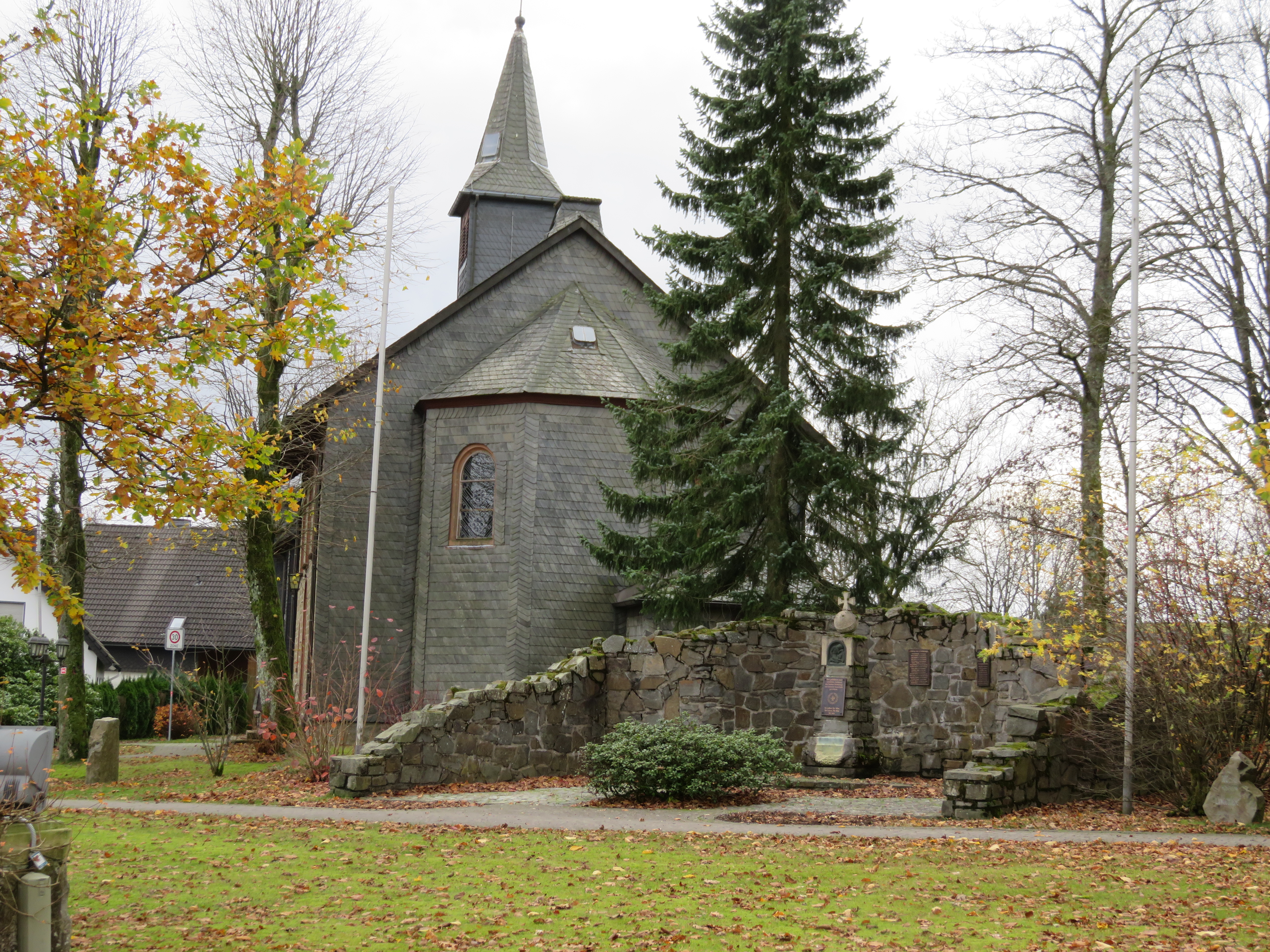 Eine Kirche umgeben von Bäumen und Wiese.
